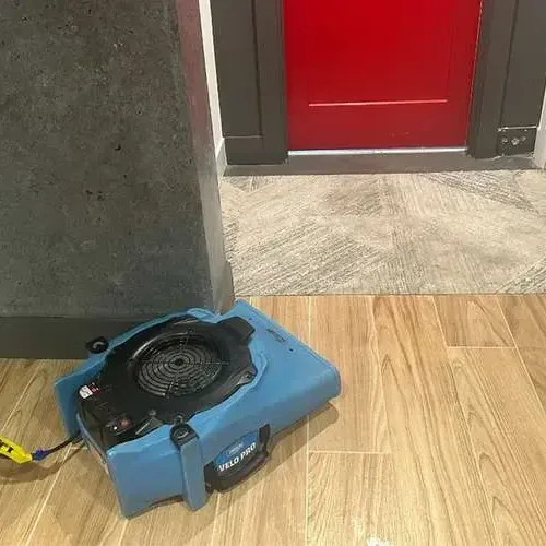 An air mover set on a wood-look tile floor next to an open doorway