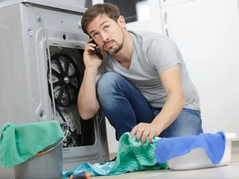A leaking washing machine with towels spread on the wet floor