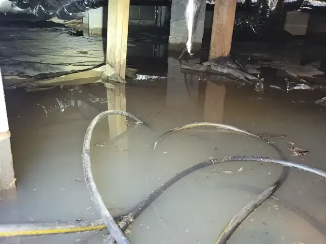 Standing water over a torn vapor barrier inside a flooded crawl space