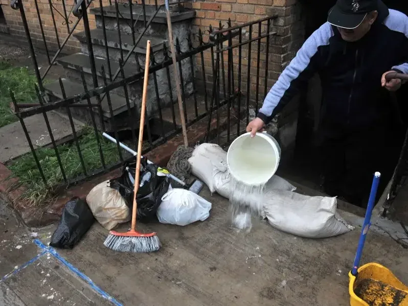 A resident bailing floodwater beside sandbags at a lower stairway